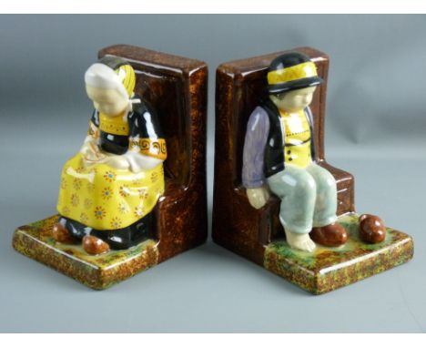 A PAIR OF QUIMPER POTTERY BOOKENDS modelled as a young girl and boy seated on benches, the girl with a bowl and spoon in hand
