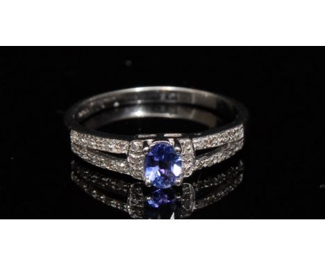 A new tanzanite and diamond ring,  central oval tanzanite, flanked by diamond encrusted open shoulders, set with fifteen diam