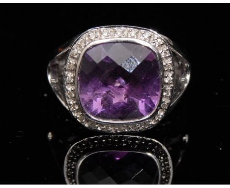 An amethyst and diamond ring, central cushion cut amethyst surrounded by a band of twenty two round cut diamond, 9ct white go