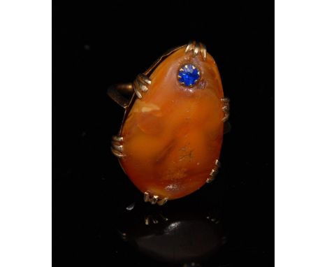 An amber and blue sapphire ring, tear drop amber cabochon, inset with a single blue sapphire, unmarked yellow metal shank, si