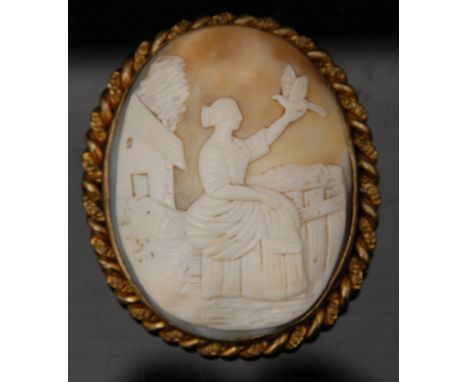 A 19th century hard shell carved cameo brooch, as a seated maiden arm aloft holding a dove,  before a farmyard and gate, gold