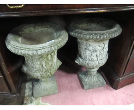 A PAIR OF COMPOSITION STONE URNS each of semi lobed campana form moulded in relief with figures raised on a square base 50cm 