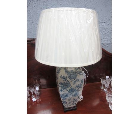 A PORCELAIN TABLE LAMP the white and blue ground decorated with flowerheads and foliage raised on a hardwood base with pleate