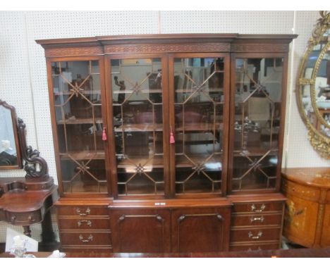 A CHIPPENDALE STYLE MAHOGANY BREAKFRONT BOOKCASE the scroll pierced pediment and blind fret frieze with astragal glazed doors