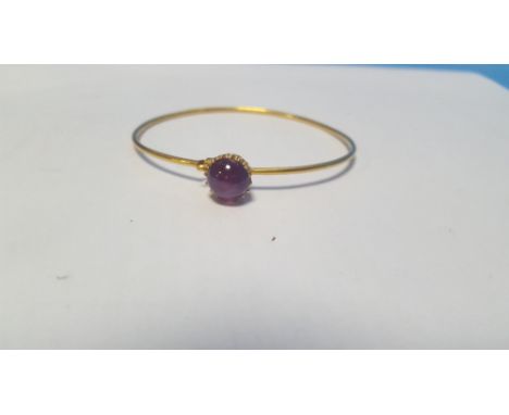 AN UNMARKED YELLOW METAL BANGLE SET WITH A PURPLE CABACHON POSSIBLY AMETHYST. Approx. weight 7.8 g