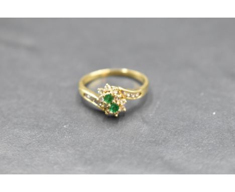 An emerald and diamond double cluster ring having diamond set cross over shoulders on an 18ct gold loop, size P &amp; approx 