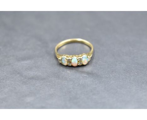 An opal and diamond ring having a trio of opal cabochons with diamond chip spacers in a gallery style mount on an 18ct gold l
