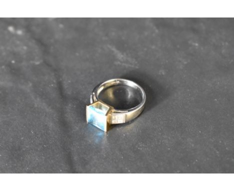 A blue topaz solitaire ring of stylised form, having a tension set princess cut convex stone in a raised yellow gold mount to