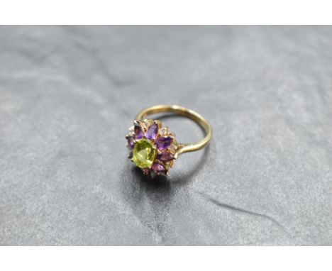 A large amethyst and diamond chip oval cluster ring with central green gem in a stepped claw set mount on a yellow metal loop
