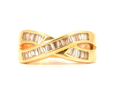 A diamond crossover ring, the twenty-seven baguette and tapered baguette diamonds channel set in a yellow metal mount size Q1