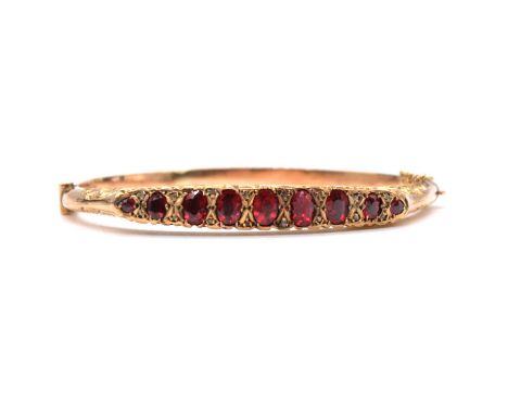 An Edwardian half hinged bangle, the nine red stones graduating in size, collet and claw set and spaced by eight pairs of dia