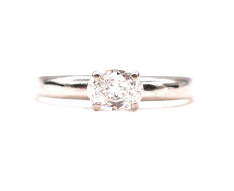 A diamond solitaire ring, the oval faceted stone claw set horizontally in an all platinum mount on a tapered D shape band rin