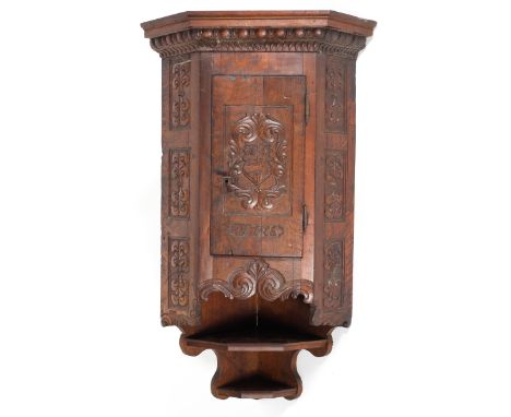 An 18th century carved walnut corner cupboard, with two shelves above a panelled door carved with the initials HIV and date 1