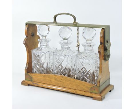 An early 20th century oak and brass mounted tantalus, with a Betjemann's patent, 47818, London, fitted with three glass decan