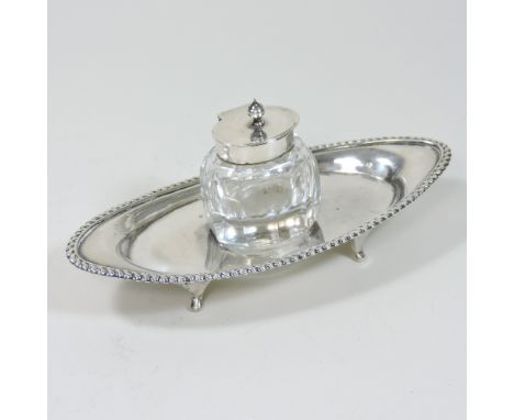 An early 20th century silver desk stand, of elliptical shape, with a gadrooned border, fitted with a silver mounted glass ink