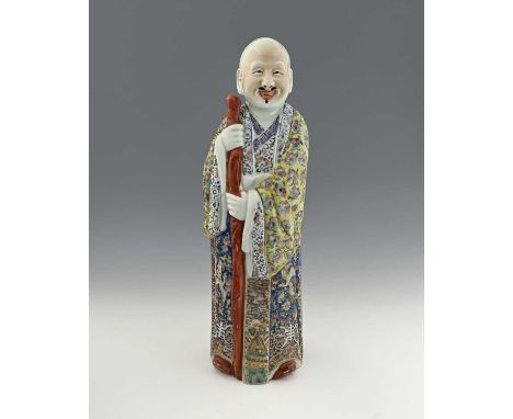A Chinese porcelain figure of an elder, modelled standing, enamelled with foliate scroll patterned robes, holding a staff, im