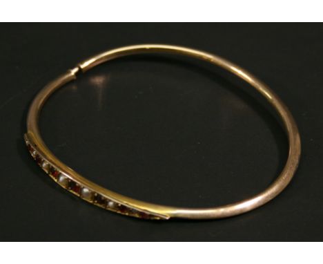 A 9CT GOLD RUBY AND PEARL BANGLE, the platform set with a linear arrangement of graduating round-cut rubies and seed pearls, 