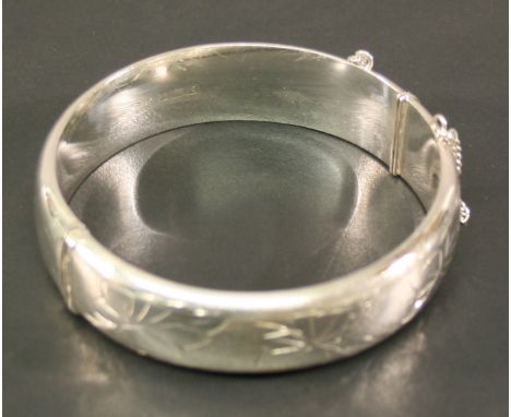 A SILVER BANGLE of hinged circular form, one side engraved with foliate decoration, marks for Birmingham 1975, maker 'E.J LD'