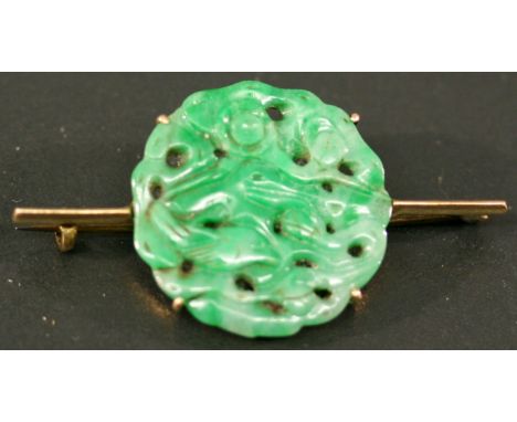 A YELLOW METAL AND JADE BROOCH, the slender bar mounted centrally with a circular jade disk, carved and pierced with birds an