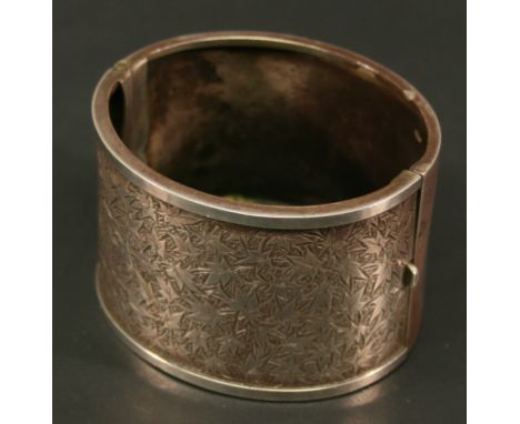 A VICTORIAN WHITE METAL BANGLE of broad hinged oval form, the front engraved with foliate decoration, unmarked, testing as si