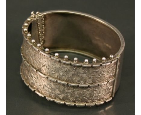 A VICTORIAN SILVER BANGLE of broad hinged oval form, the front with engraved foliate decoration and central division, between