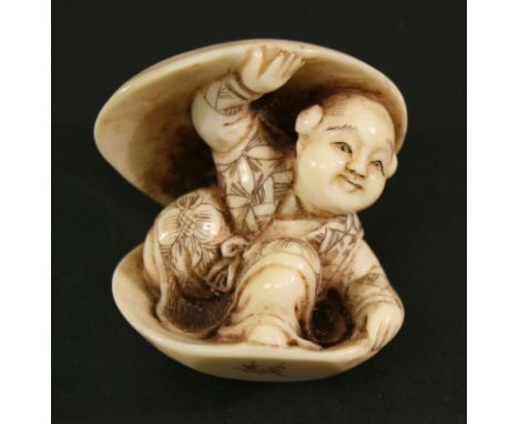  A JAPANESE CARVED IVORY NETSUKE early 20th century, carved as a mischievous young boy seated within a clam shell, signed to 