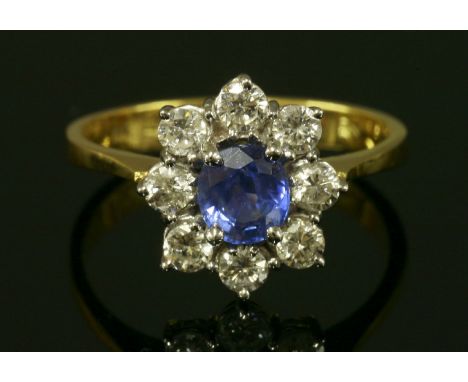 An 18ct gold sapphire and diamond cluster ring, with an oval mixed cut sapphire, four claw set and surrounded by brilliant cu