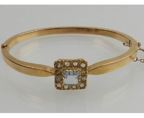A yellow gold, diamond, and aquamarine bangle, set square cut aquamarine surrounded by twelve old cut diamonds. 