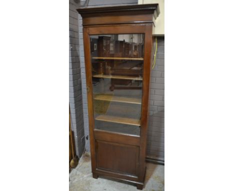 An Edwardian mahogany floorstanding cabinet enclosed by a long glazed and part panelled door below a dentil cornice on bracke