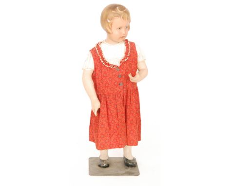 A 1930s/40s shop display child mannequin known as 'Daphne' with painted composition features and faux hair in a red buttoned 