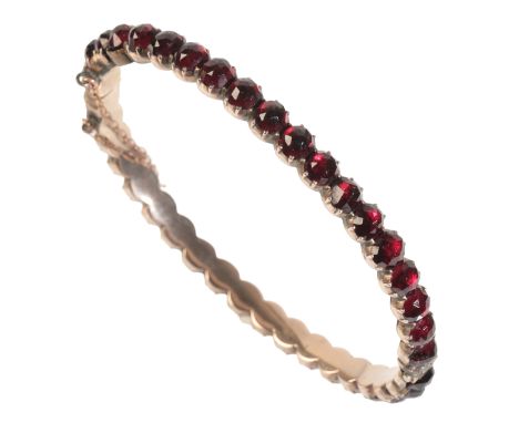 AN EDWARDIAN ROSE CUT GARNET BANGLE consisting of twenty eight garnets with good lustre, hinged with safety chain, Edwardian 
