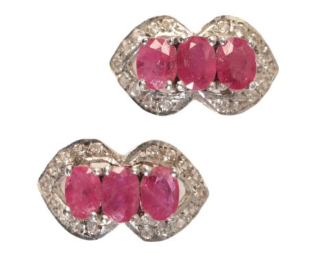 A PAIR OF RUBY AND DIAMOND EARRINGS of oval, curved outline, white gold coloured metal settings, each with three rubies withi