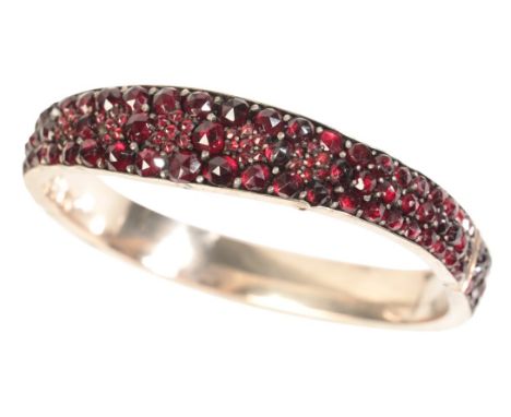 A GARNET AND SILVER COLOURED BANGLE with deep red rose cut garnets, snap shut fastening with safety chain, gross weight circa