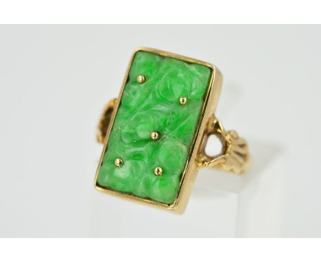 A 9CT GOLD JADE RING, designed as a rectangular carved panel of jade within a rectangular collet setting, to the bifrucated s