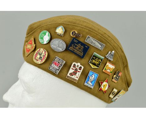 A WWII ERA STYLE RUSSIAN SIDE CAP, with a number of enamel and metal pin badges affixed 38 in number