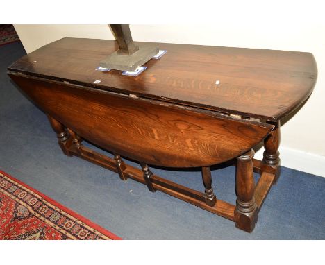 A REPRODUCTION GEORGE III STYLE OAK WAKE TABLE, the two rounded drop leaves to form an oval supported by four pivoting gate l