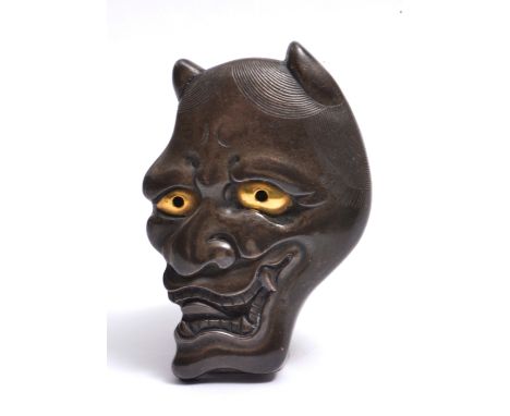 A JAPANESE SHIBUICHI NETSUKE modelled as a mask of Hannya, eyes in gold, reverse with a centrally placed ring and floret, him
