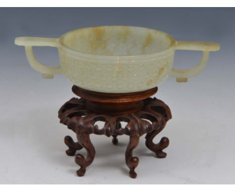 A CHINESE PALE CELADON JADE MING STYLE TWO HANDLED WINE BOWL with raised rice grain pattern, 18th Century, on a hardwood stan