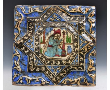 A PERSIAN BLUE GROUND QAJAR TILE, the central panel having a figure holding an opium pipe within a relief moulded surround an