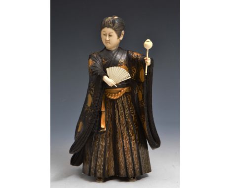 A JAPANESE WOOD AND IVORY OKIMONO of a young actor performing a dance while holding an open fan and a rattle, the fine robes 