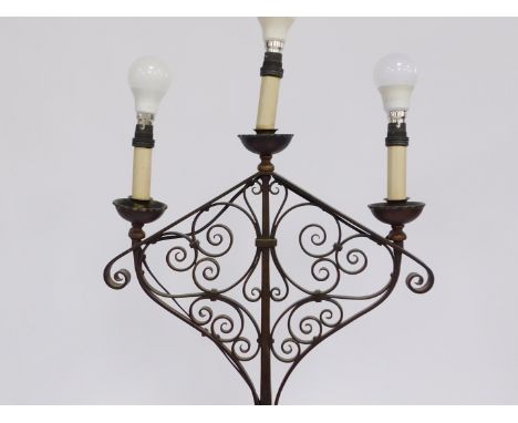 A wrought iron standard lamp, with a three arched candelabrum top, converted to electricity, 165cm high.WARNING! This lot con