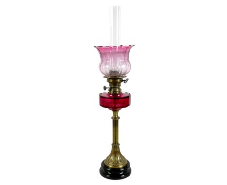 A Victorian paraffin lamp, with rose glass reservoir on a brass column and black ceramic circular socle base, etched rose pin