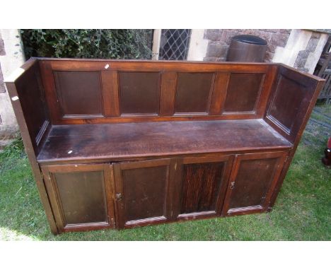 An oak settle/hall bench with panelled frame, partially enclosed by four doors, 146 cm long x 40 cm wide x 95 cm high 