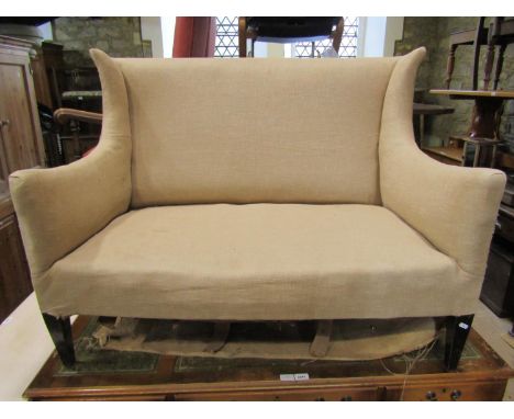 An Edwardian two seat sofa with shallow winged back, simply upholstered in oatmeal fabric and raised on square tapered suppor