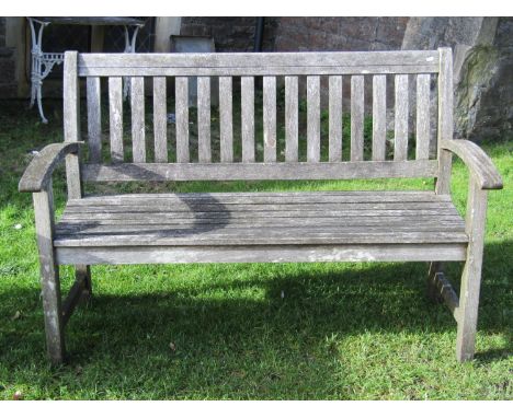 A weathered contemporary teak two seat garden bench with slatted seat and slightly curved slatted back and arms, approx 140 c