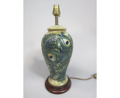 A Moorcroft ceramic lamp base, with painted and moulded peacock feather design in the art nouveau manner, raised on a wooden 