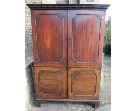 A Georgian mahogany dwarf robe enclosed by a pair of moulded panelled doors beneath a dentil cornice and raised on bracket fe