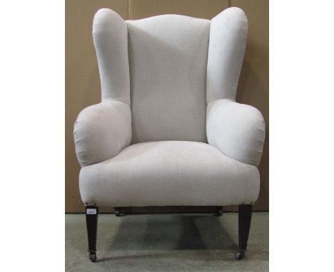 An Edwardian wing armchair with simply upholstered light oatmeal fabric and raised on square tapered forelegs with brown cera