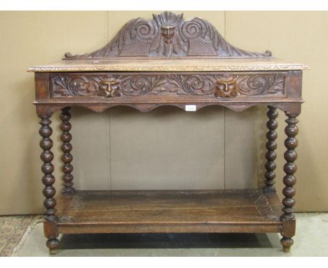 A Victorian gothic oak side table with carved acanthus and face mask detail, scrolled back, frieze drawer on turned bobbin su