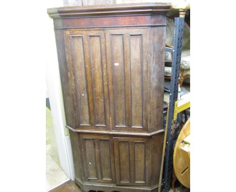 A substantial Georgian oak free standing corner cupboard enclosed by two pairs of panelled doors and raised on bracket suppor